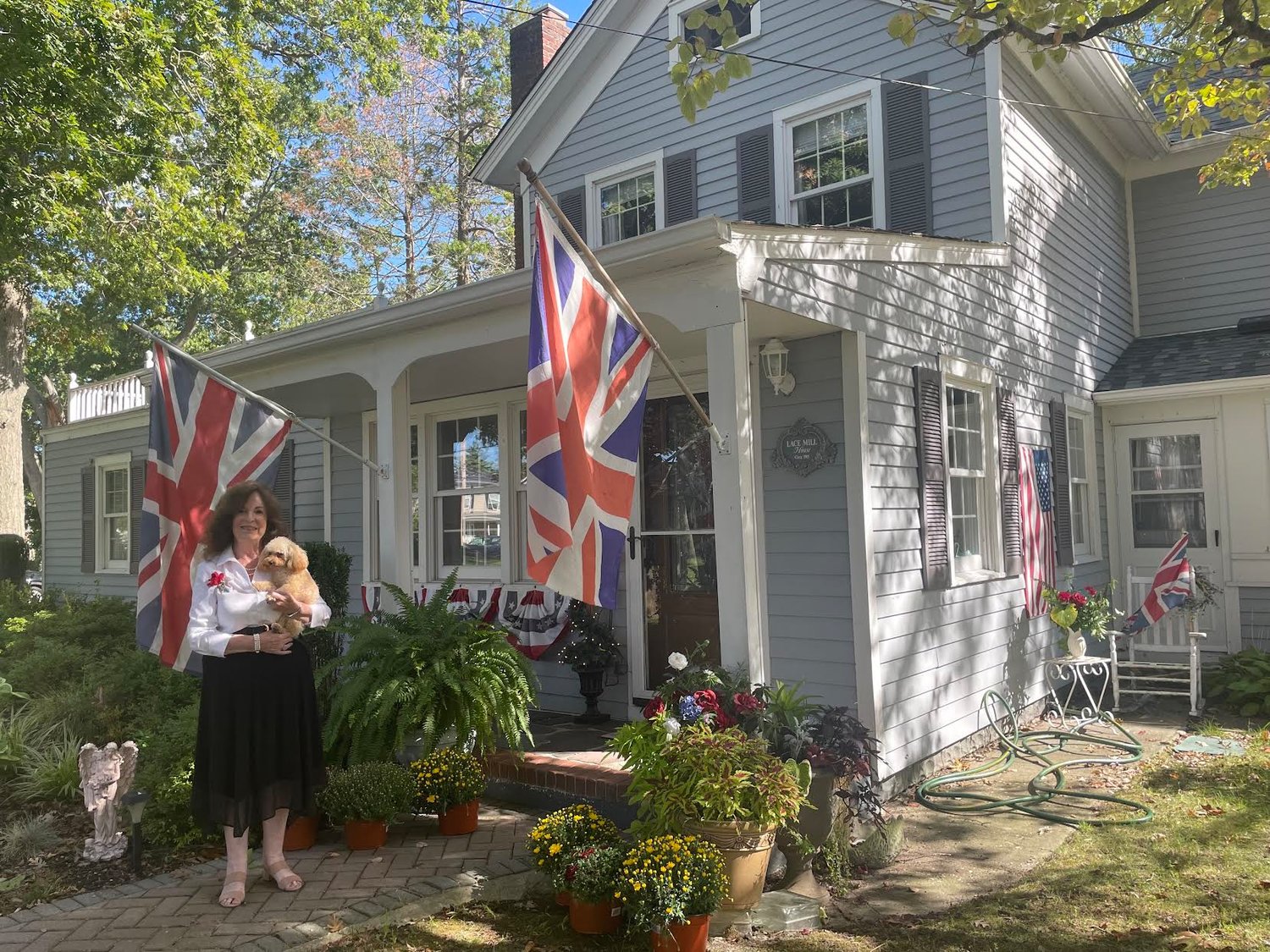 Pictured is England native Penelope Grippo, 77, outside her decorated home in honor of the queen at 99 Lake Shore Drive in Patchogue with her dog Paddington the toy poodle. She is sporting her crystal-adorned red poppy on her chest in honor of her late father who gave it to her to match the queen’s diamond-adorned poppy.
